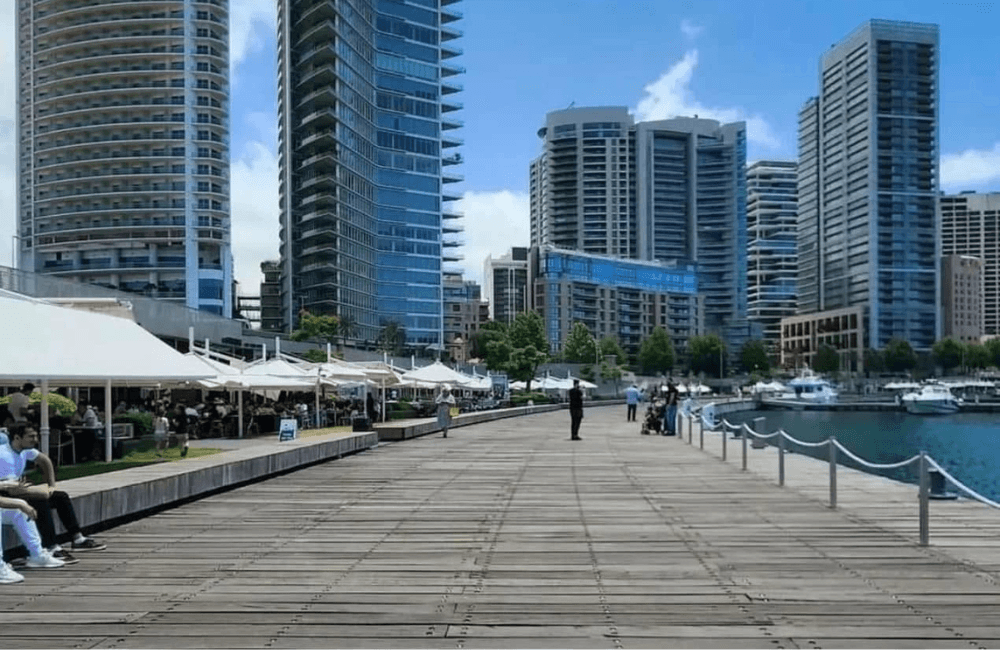 Waterfront boardwalk at Beirut's Zaitunay Bay lined with modern high-rise towers, cafes, and moored boats on a clear day, reflecting Lebanon's real estate market.