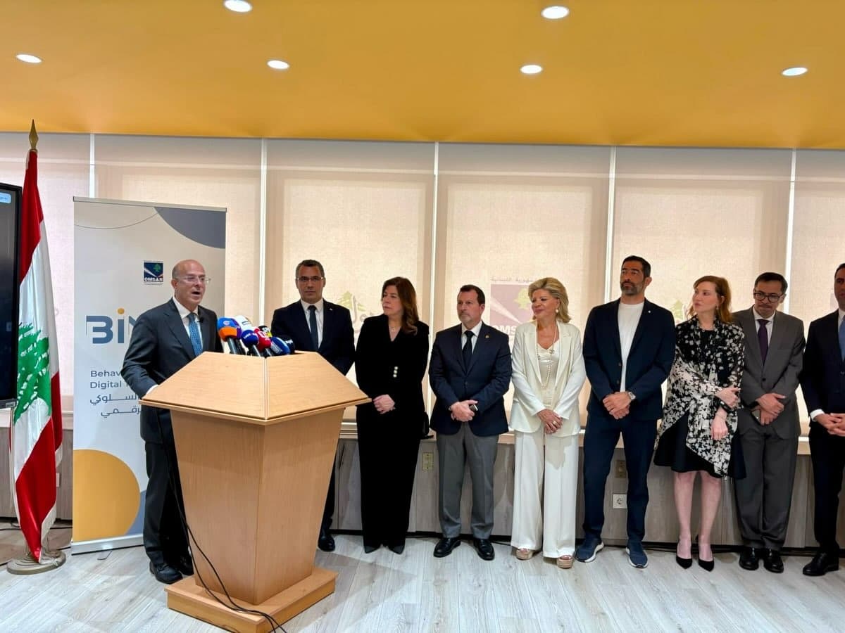 Minister of Administrative Development Fadi Makki speaks at a podium with press microphones during the Dawlati platform launch, standing beside the Lebanese flag and an OMSAR banner, with nine officials lined up to his side.