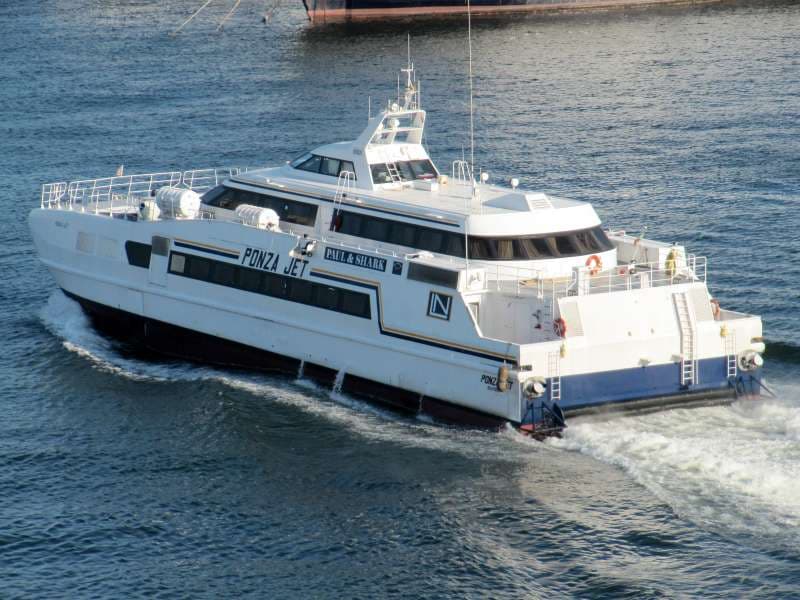 A white high-speed passenger catamaran ferry cutting through deep blue open water at speed