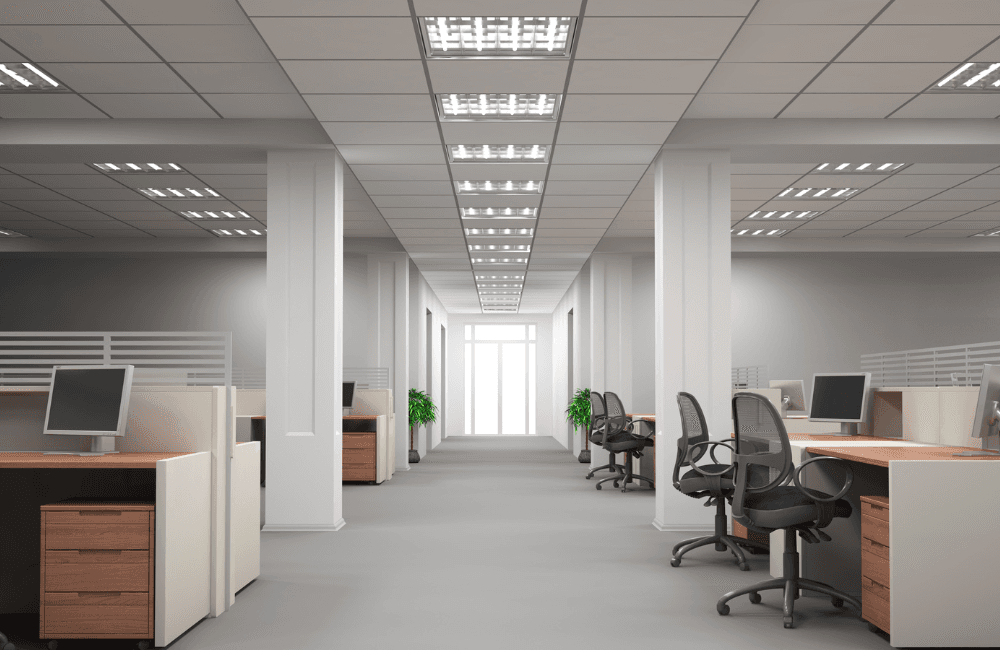 An empty open-plan office with rows of workstations, computer monitors, and vacant office chairs