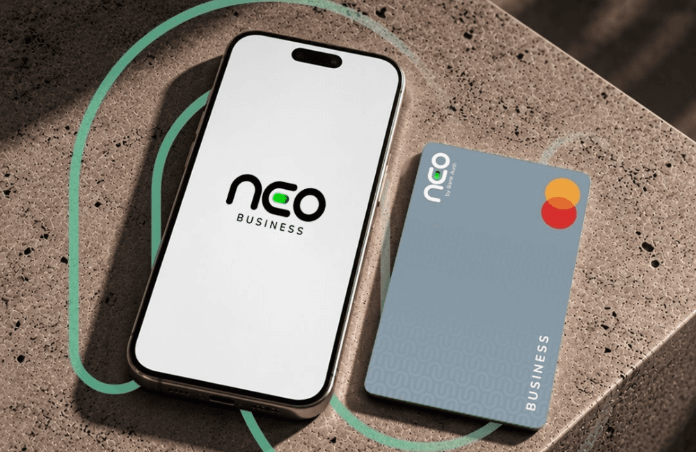 A smartphone displaying the neo Business logo beside a grey neo by Bank Audi Mastercard business debit card on a stone surface